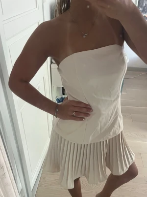 Champagnefärgad axelbandslös klänning - Snygg axelbandslös klänning i champagnefärg med.Perfekt för dig som vill sticka ut med en elegant och modern look. Ny och oanvänd!!