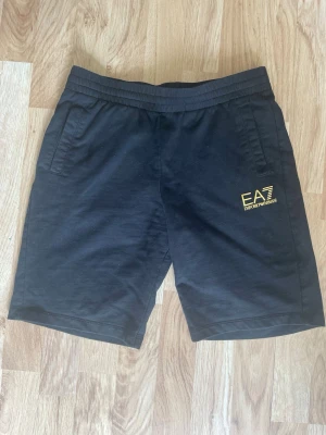 Svarta shorts från Emporio Armani strl 160  - Snygga svarta shorts från Emporio Armani EA7 med gul logga på vänster ben. Shortsen har använts ett par ggr strl 160 
