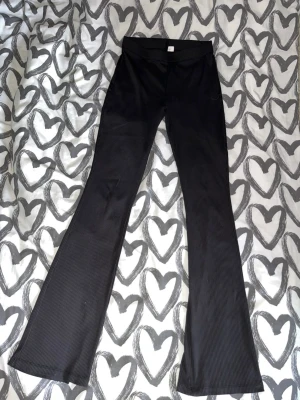 Bootcut leggings - Säljer ett par svarta leggings med tunna ränder och bootcut-ben. De har hög midja och stretchigt material som sitter skönt. Perfekta för dig som gillar en enkel men trendig look.
