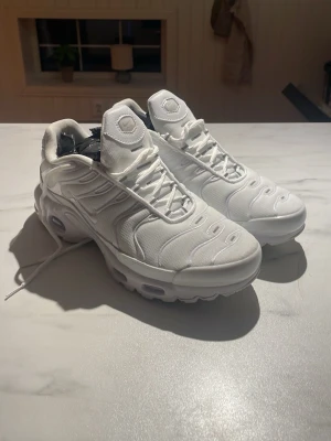 Nike tn tripple white - Snygga helvita sneakers med chunky sula och tydliga luftbubblor i sulan. Skorna har en sportig design med vågiga detaljer på ovandelen och är tillverkade i textil och syntetmaterial. Perfekta för dig som gillar en clean och modern look.