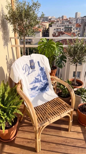 Vit t-shirt med blått tryck - Vit t-shirt med stort blått tryck framtill som föreställer en vinflaska, glas och texten 'Dolce Litu'. Klassisk passform och rund hals. Perfekt för dig som gillar stilrena men ändå unika plagg.