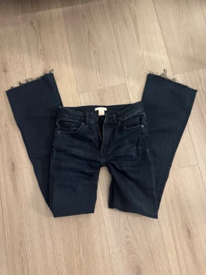 Mörkblå bootcut jeans  - Säljer ett par mörkblå bootcut jeans med råa, fransiga benslut. Jeansen har klassisk femficksmodell, dragkedja och knapp i midjan. 