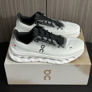 Vita sneakers med svart detalj - Snygga vita sneakers med svarta detaljer och logga på sidan. Skorna har en unik sula med hål och mesh-ovandel för bra ventilation. Perfekta för dig som gillar sportig och modern stil.