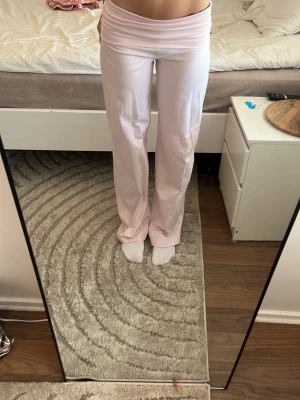 Ljusrosa yogapants - Säljer ett par ljusrosa mjukisbyxor med bred, vikbar linning och raka ben. Byxorna har en relaxed fit och är perfekta för chill dagar. Tillverkade i ett mjukt och stretchigt material som känns skönt mot huden. Passar dig som gillar en enkel och clean stil.