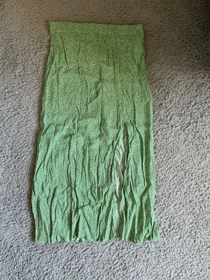 Grön blommig kjol från H&M - Snygg grön kjol från H&M med små vita blommor och svart detalj. Kjolen har en kort längd och är perfekt för dig som gillar en feminin och trendig stil. Tillverkad i ett lätt och bekvämt material som passar bra till varmare dagar. Passar S också