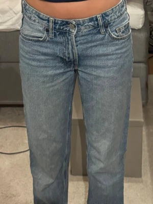 Blå raka jeans med hög midja - Säljer ett par klassiska blå jeans med rak passform och hög midja. Jeansen har fem fickor, bälteshällor och stängs med knapp och dragkedja. Tillverkade i ett slitstarkt denimtyg som ger en tidlös look.