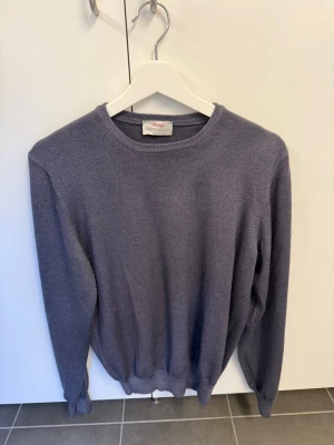 Blå stickad tröja Gran Sasso i 100% Virgin Wool, stl 46/S - Säljer en stilren blå stickad tröja från Gran Sasso. Tröjan har rund halsringning, långa ärmar och ribbade muddar vid ärmslut och nederkant. Tillverkad i Italien och har en klassisk, enkel design som passar till mycket.