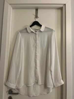 Vit långärmad blus från Soyaconcept - Stilren vit blus från Soyaconcept med klassisk krage och knäppning framtill. Blusen har lång ärm och är tillverkad i ett tunt, lätt material som ger ett snyggt fall. Perfekt att matcha med jeans eller kjol för en clean look.
