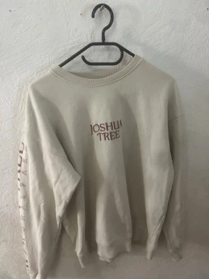 Beige sweatshirt Joshua Tree tryck - Cool beige sweatshirt med trycket 'Joshua Tree' fram och stort färgglatt motiv på ryggen. Tryck även längs ena ärmen. Oversized passform med ribbade muddar vid hals, ärmslut och nederkant.