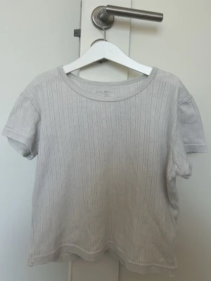 Ljusribbad kortärmad t-shirt - En ljus, ribbad t-shirt med korta ärmar och rund hals. Från Brandy Melville. T-shirten har ett diskret mönster i tyget och är tillverkad i mjuk bomull, perfekt för en avslappnad och enkel stil.