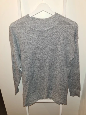 Grå stickad tröja från 157 - Mysig grå stickad tröja från 157 med rund halsringning och ribbade muddar vid ärmslut och nederkant. Perfekt för kyliga dagar och enkel att matcha med olika outfits. Materialet känns mjukt och bekvämt mot huden.