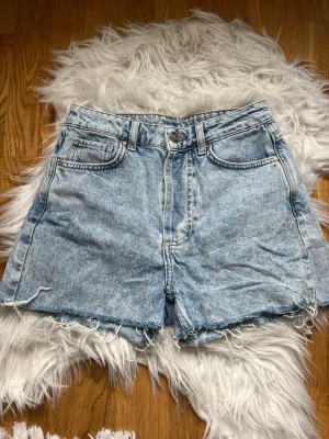 Ljusblå jeansshorts - Säljer ett par ljusblå jeansshorts som ät i väldigt bra skick och har en lite sliten look vid byxbenen. De är 100% bomull. Skriv för mått! 