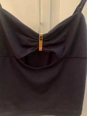 Marinblå croppad linnetopp med cut-out - Trendig svart croppad linnetopp med smala axelband och en snygg cutrr-out detalj framtill. Toppen har en guldfärgad metallbit vid bysten som ger en extra touch. Perfekt för dig som vill ha en enkel men ändå unik topp till sommaren.passar även för small