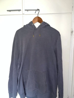 Mörkgrå hoodie med ficka - En enkel och stilren mörkgrå hoodie med huva och dragsnören. Hoodien har en stor känguruficka framtill och ribbade muddar vid ärmslut och nederkant. Perfekt för en avslappnad och chill look. Materialet känns mjukt och bekvämt.