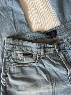 Ljusblå raka jeans med slitningar - Säljer ett par ljusblå jeans med raka ben och snygga slitningar. Klassisk femficksmodell med bälteshällor och dragkedjegylf. Jeansen har en avslappnad passform och är tillverkade i denim med tvättad look.