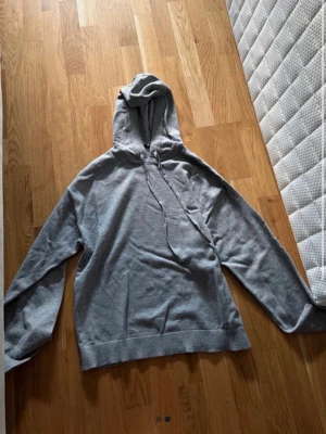 Grått loungewear-set med hoodie - Mysigt loungewear-set i mjukt grått material. Setet består av en hoodie med dragsko och långa ärmar samt ett par vida byxor med resår och dragsko i midjan. Perfekt för chill dagar hemma eller när du vill vara extra bekväm.