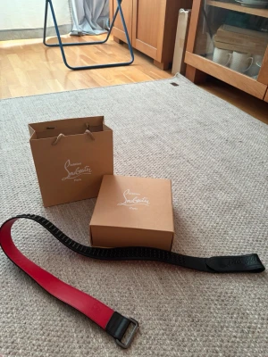 Svart och rött skärp från Louboutin - Snyggt skärp från Louboutin i svart skinn med röd insida och präglad logga på lädret. Perfekt accessoar för att lyfta din outfit med en lyxig touch. Kommer med originalförpackning och påse.