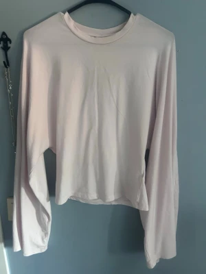 Ljusrosa långärmad croppad topp - En enkel och stilren ljusrosa långärmad topp med croppad passform. Tillverkad i mjukt bomullstyg och har en klassisk rund halsringning. Perfekt att matcha med höga jeans eller kjol för en clean look.