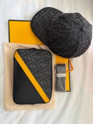 Fendi svart axelväska med gul detalj - Snygg svart axelväska från Fendi med klassiskt FF-mönster och en diagonal gul skinnrem på framsidan. Väskan har en rektangulär form och är tillverkad i canvas och läder. Perfekt för dig som gillar statement-accessoarer. Skriv dm för beställning.