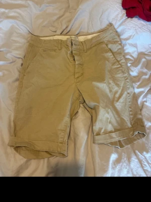 Beige shorts från Jack & Jones - Snygga beige shorts från Jack & Jones med klassisk passform och knappgylf. Tillverkade i mjuk bomull, perfekta för varma dagar. Shortsen har fickor fram och bak samt diskreta sömdetaljer för en clean look. Säljer dom på vinted därav att de står stäng osv