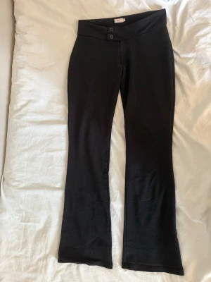 Svarta bootcut kostymbyxor/leggings från Nelly - Snygga svarta leggings från Nelly med bootcut-modell och hög midja. De har två knappar framtill och är tillverkade i ett stretchigt material som sitter bekvämt. Ser ut som kostymbyxor men har leggings material.