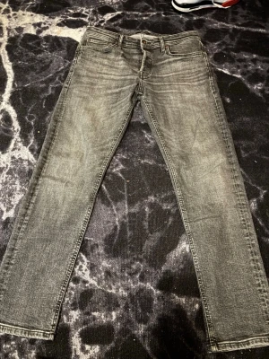 Grå slim fit jeans med tvättad look - Jack & Jones Mike Tapered jeans i storlek W33/L32. Bra begagnat skick utan hål eller fläckar. Grå/svart tvätt med normal passform och avsmalnande ben. Skickas snabbt.