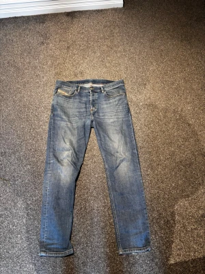 Blå raka jeans från Diesel - Säljer ett par klassiska blå jeans från Diesel med raka ben och snygg slitning. Jeansen har fem fickor och detaljerade sömmar. Perfekta för dig som gillar en avslappnad men ändå stilren look.