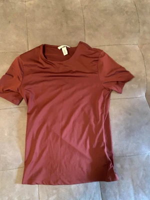 Mörkröd basic t-shirt från H&M - En enkel och stilren mörkröd t-shirt från H&M. T-shirten har rund halsringning och korta ärmar. Tillverkad i mjuk bomull som känns skön mot huden. Perfekt att matcha med jeans eller shorts för en clean look.