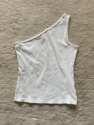 Vit oneshoulder topp - Snygg vit oneshoulder topp i ribbad bomull. Enkel och stilren design med asymmetrisk axel.