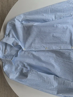 Blåvit randig skjorta från Zara - Klassisk blåvit randig skjorta från Zara i bomull. Skjortan har långa ärmar, knappar framtill och en avslappnad passform. Perfekt för en clean och stilren look. Använd 3 gånger.