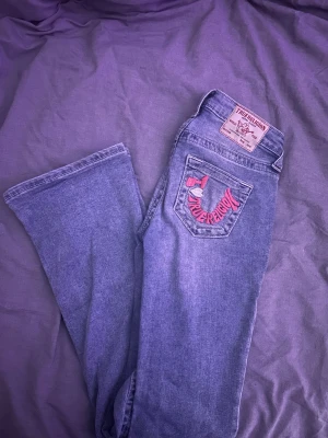 Blå bootcut jeans True Religion - Säljer ett par ljusblå bootcut jeans från True Religion med broderi på bakfickorna. Jeansen är i modellen Becca och är mid waist. 