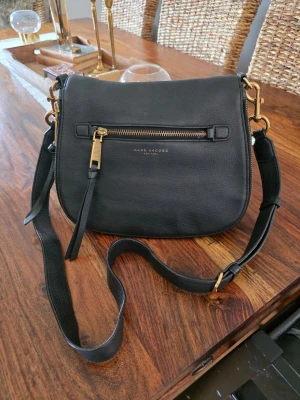 Marc Jacobs - Snygg svart axelväska från Marc Jacobs i äkta läder med guldfärgade detaljer och dragkedja framtill. Perfekt för dig som vill ha en trendig och praktisk väska. Väskan är i fint skick 