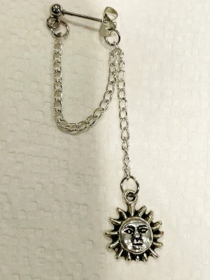 By prisförslag- 1 st Silvrigt örhänge med solformad berlock - Unikt silvrigt örhänge med kedja och solformad berlock. Örhänget har en säkerhetsnål-design och två kedjor som ger en cool och edgy look. Berlocken är i metall och har en detaljerad solform. Perfekt för dig som vill sticka ut med dina accessoarer.