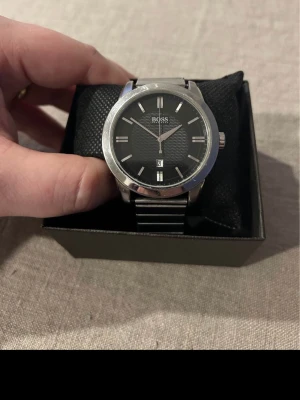 Hugo Boss 44mm Herrklocka - Säljer en mycket snygg stilren herrklocka från Hugo Boss i nära nyskick. Endat några få hårfina repor som ej stör eller syns. Går bra, långt armband i stål (ej original), datumvisare, vattentät osv. Behöver bara nytt batteri.   Nypris: 3300 SEK Begagnat pris: 1000-1500 SEK Mitt pris: 589 SEK  Skickas alltid spårbart och snabbt (ofta samma dag) eller hämtas i Glumslöv.  Hör av dig vid frågor och se gärna mina andra annonser också!   Manufacturer - Brand: BOSS Type of goods: Men's watches Technolo