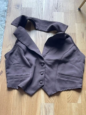Brun halterneck väst med knappar - Brun väst med halterneck och bred krage. Croppad modell.