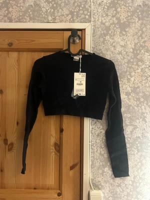 Svart croppad långärmad topp - Svart ribbad croppad långarmad topp från Zara. Helt oanvänd med prislapp kvar. Hör av vid frågor!💗