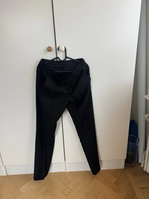 Svarta kostymbyxor J.Lindeberg  - Snygga svarta kostymbyxor med raka ben och pressveck. Klassisk design med hällor för skärp och diskret knappstängning. Perfekta för en fine look och passar till skjorta eller t-shirt. Materialet ser ut att vara en blandning av polyester och viskos. Mycket bra skick 9/10 nypris 1600 kr 