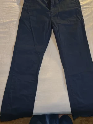 Mörkblå Gant chinos i rak modell - Snygga mörkblå chinos från gant med rak passform och klassisk design. Byxorna har diskreta fickor och stängs med knapp och dragkedja. Tillverkade i ett mjukt bomullstyg som ger en bekväm känsla hela dagen.