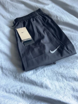 Svarta Nike shorts med logga - Snygga svarta shorts från Nike med vit logga på benet. Shortsen har elastisk midja med snörning och är tillverkade i ett lätt och bekvämt material, perfekta för träning eller chill. Klassisk och stilren design som funkar till det mesta.