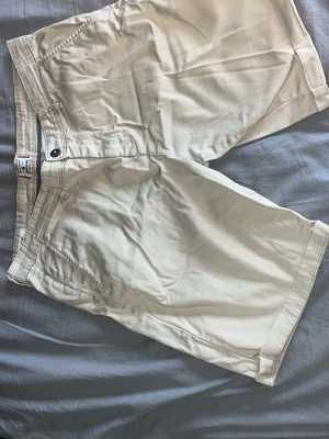 Beige shorts från Jack and Jones - Klassiska beige shorts från Jack and Jones med normal passform. Tillverkade i bomull med knapp och dragkedja framtill, samt fickor både fram och bak. Perfekta för varma dagar och enkel att matcha med olika stilar.