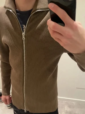 Brun ziptröja  - Säljer en brun ribbad tröja med dragkedja framtill och hög krage. Tröjan har långa ärmar och är tillverkad i ett mjukt stickat material. Perfekt för lager på lager och enkel att matcha med olika outfits. Skriv om ni har frågor 😁