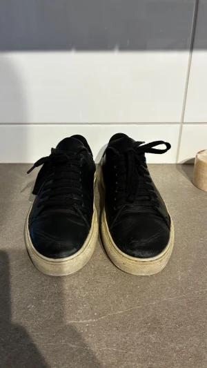 Svarta låga sneakers i läder - Stilrena svarta sneakers i läder med vita sulor och svarta skosnören. Klassisk låg modell som passar till det mesta. Dem är sparsamt använda!