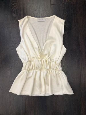 Vit omlottopp från Anna Field - Snygg vit omlottopp från Anna Field i ett mjukt och lätt material. Toppen är ärmlös med v-ringning och har resår i midjan som ger en fin siluett. Perfekt att styla med jeans eller kjol för en trendig look.