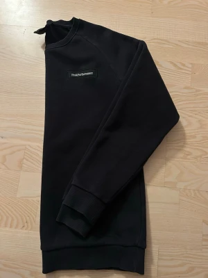 Svart sweatshirt från Peak Performance - Snygg svart sweatshirt från Peak Performance med diskret logga på bröstet. Klassisk rak passform, rund halsringning och ribbade muddar vid ärmslut och nederkant. Perfekt för en clean och stilren look.