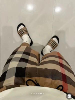 Burberry sandaler med rutigt mönster - Säljer ett par klassiska sandaler från Burberry med det ikoniska beige, svarta och röda rutmönstret. Sandalerna har svart sula och bred rem över foten. Perfekta för sommaren eller att chilla hemma. Boxen från Burberry medföljer.