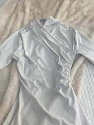 Ljus omlottklänning från H&M XS - Säljer en elegant ljus tröja från H&M i storlek XS. Tröjan har lång ärm, draperad omlottdesign och mjukt, glansigt material som ger en lyxig känsla. Perfekt för dig som gillar stilrena och moderna plagg.