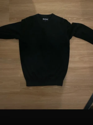 Svart tröja från Barbour - Klassisk svart  tröja från Barbour med rund halsringning och diskret broderad logga på bröstet. Tröjan har ribbade muddar vid ärmslut och nederkant. Perfekt basplagg i garderoben för en stilren look.