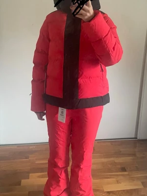 Skidkläder - Säljer ett helt oanvänt skidset från 8848 Altitude i färgen Poinsetta Red. Setet består av skidjacka och hängselbyxa. Aldrig använt och lapparna sitter kvar.  Väldigt fint och kvalitativt skidset som passar perfekt till skidåkning eller andra vinteraktiviteter.  Storlek: Storlek 170, men passar även vuxen. Jag bär vanligtvis XS/S och setet sitter perfekt på mig.  Ingår: • 8848 Altitude Moon JR Ski Jacket • 8848 Altitude Ella JR Bib Pant  Färg: röd med svarta detaljer  Skick: * Helt nytt * Aldrig