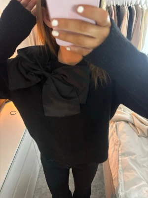 cool svart stickad tröja - säljer en as cool svart stickad tröja med en stor svart rosett framtill. perfekt för att vara lite unik!