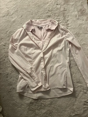 Ljusrosa skjorta med krage och knappar - Säljer en stilren ljusrosa skjorta med klassisk krage och knäppning framtill. Skjortan har lång ärm och är tillverkad i ett mjukt bomullsmaterial. Perfekt för dig som gillar en clean och enkel look. Det är två delar men köpte det som ett sett och säljer det vidare som ett sett